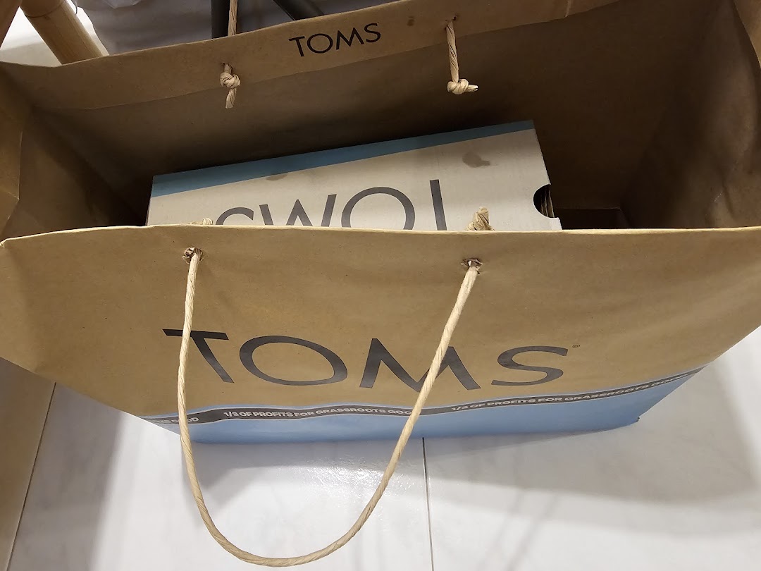 A brown TOMS shopping bag with a shoe box inside, highlighting the brand's social mission.
