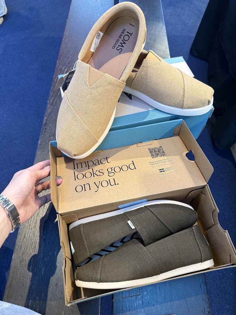 Two pairs of comfortable Toms shoes, one beige and one olive, displayed with their box.
