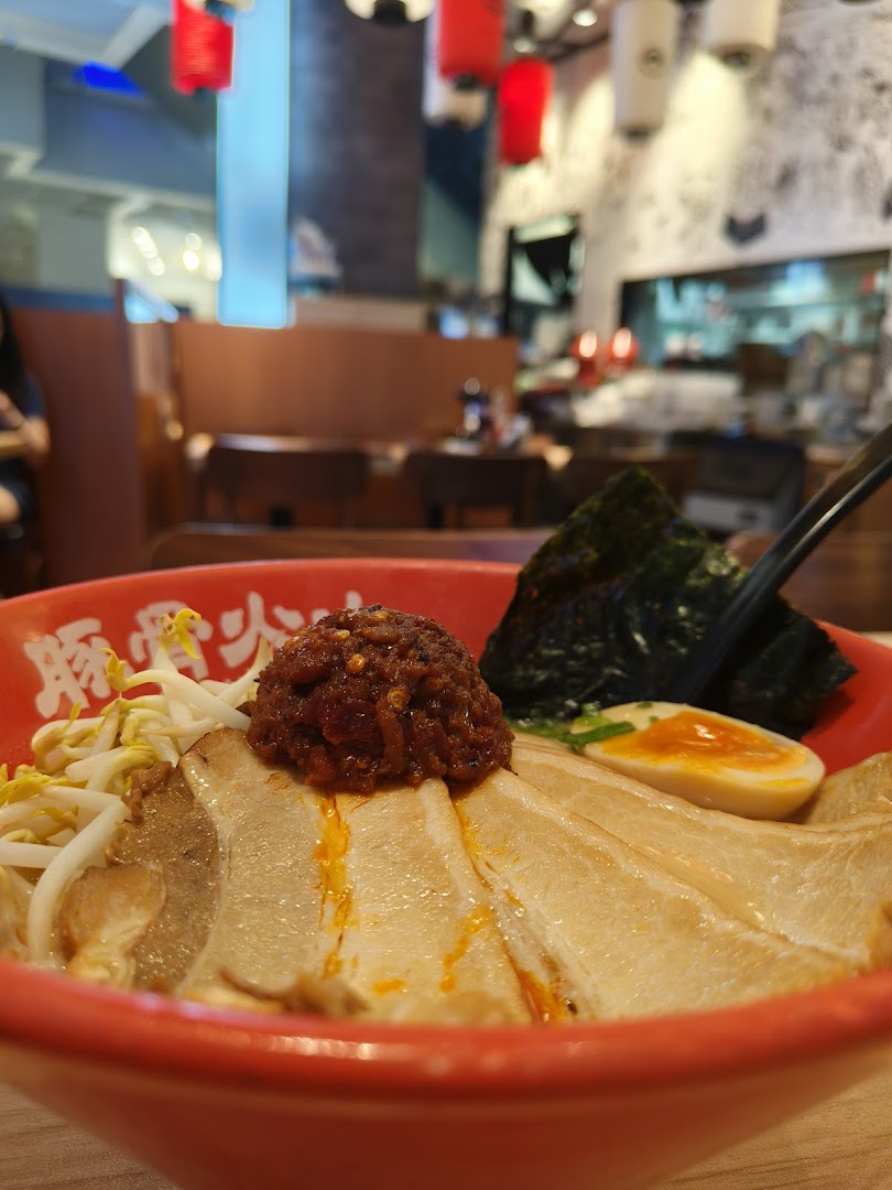 A close-up of a delicious ramen bowl with pork slices, egg, and chili paste, set in a vibrant ramen shop interior.