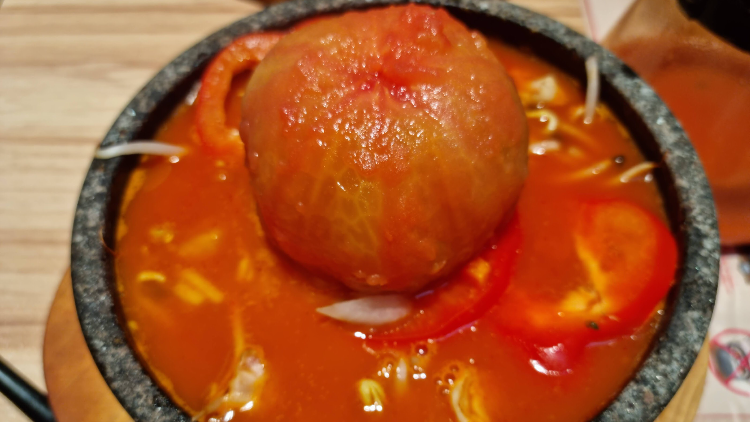 A vibrant close-up of a hot stone bowl dish featuring a whole tomato and red peppers.