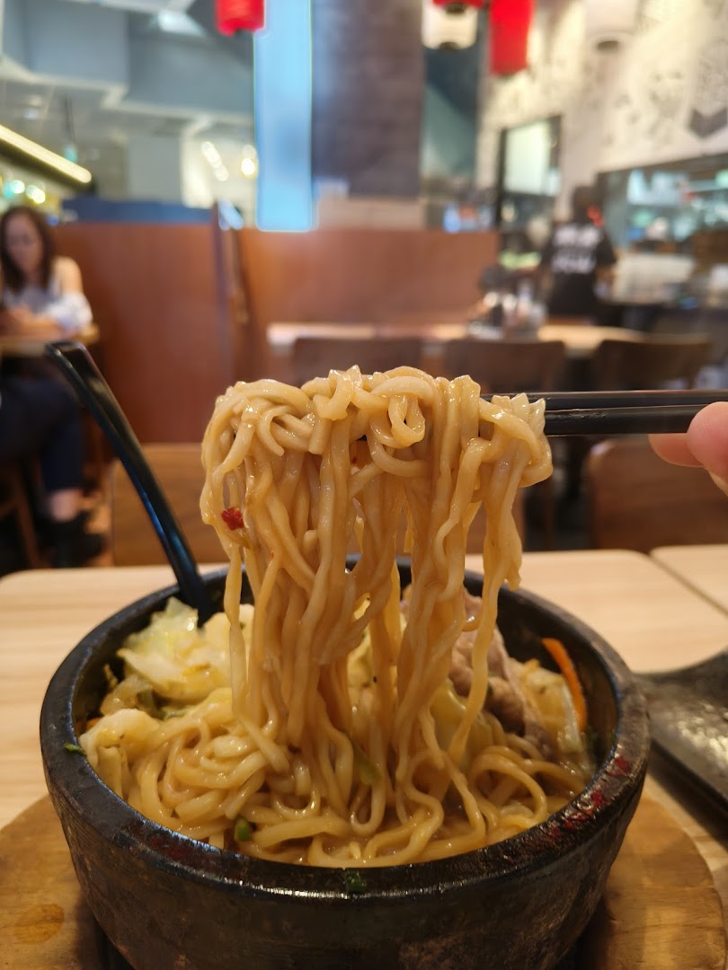 Chopsticks lift steaming ramen noodles from a hot stone bowl, showcasing a delicious meal at Tonkotsu Kazan.