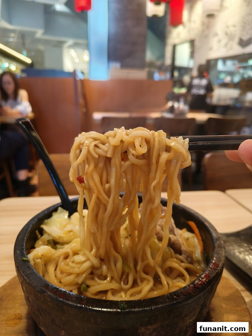 Chopsticks lift steaming ramen noodles from a hot stone bowl, showcasing a delicious meal at Tonkotsu Kazan.