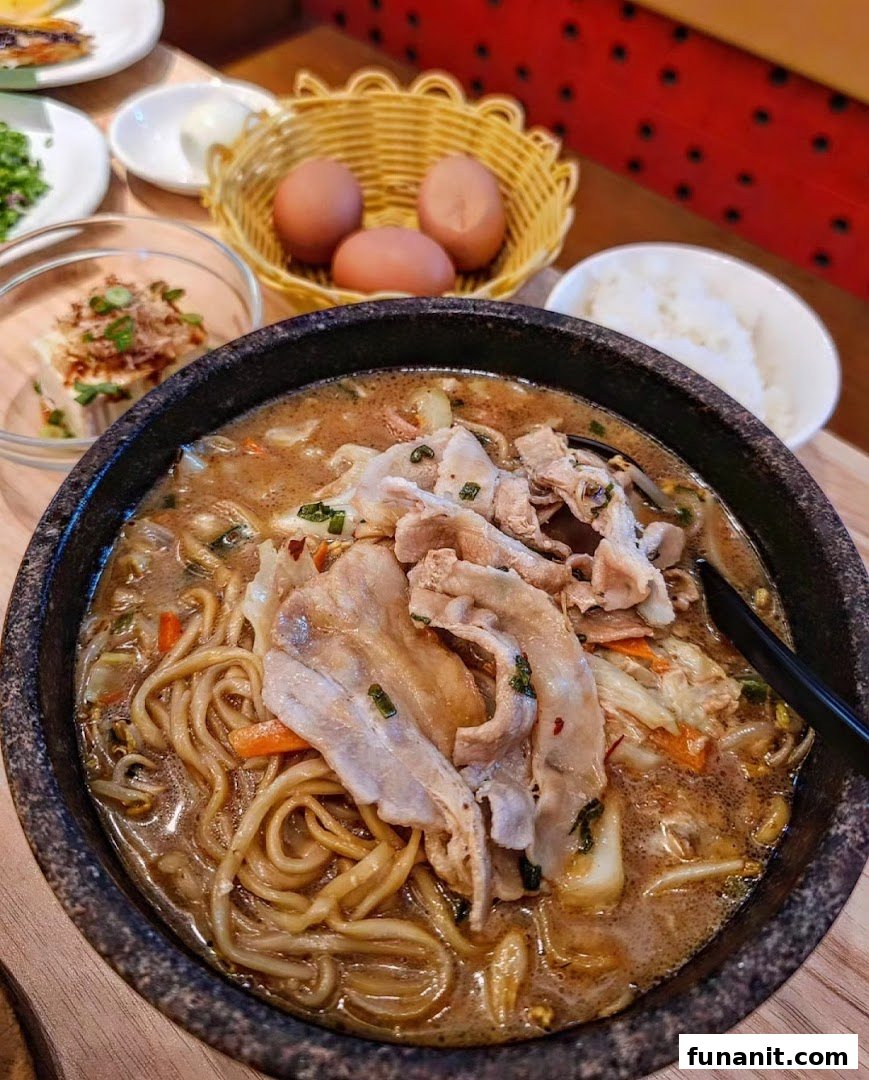 A steaming bowl of Tonkotsu Kazan ramen with pork slices, noodles, and vegetables, served with side dishes.