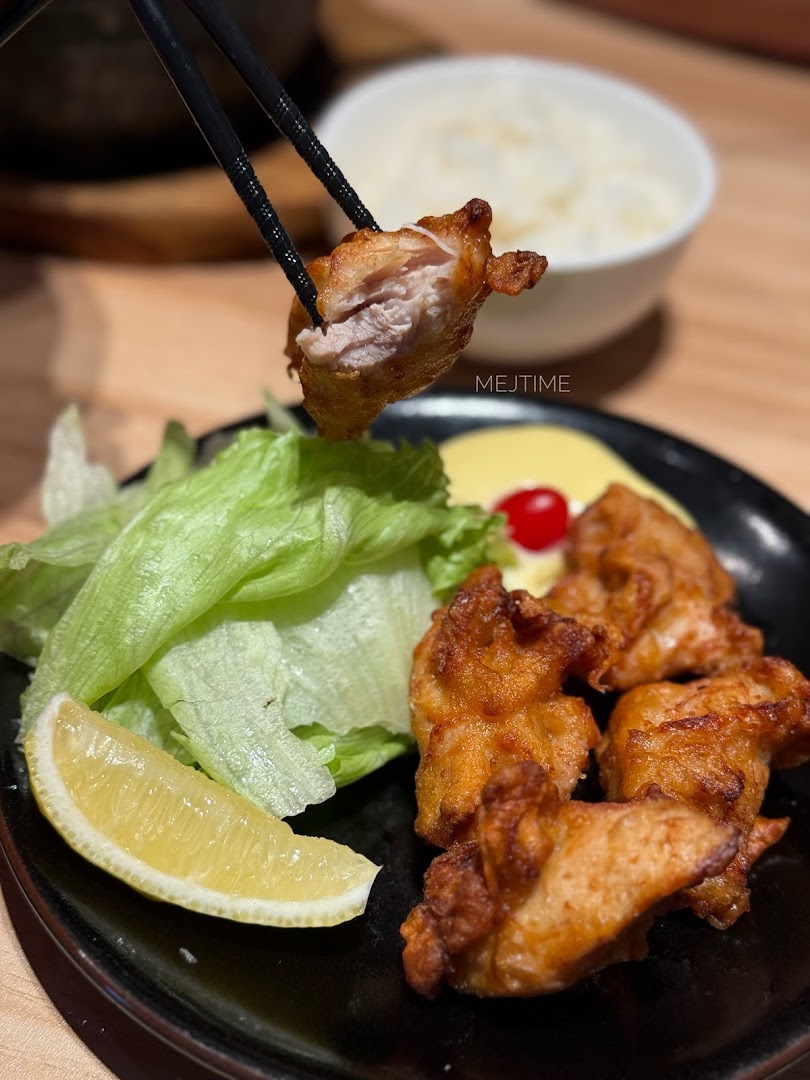 Chopsticks lift a piece of crispy Japanese fried chicken (karaage) from a plate with lettuce and lemon.