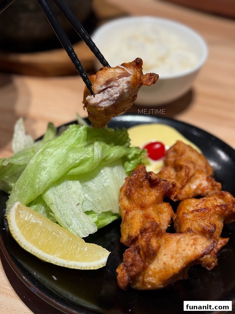 Chopsticks lift a piece of crispy Japanese fried chicken (karaage) from a plate with lettuce and lemon.