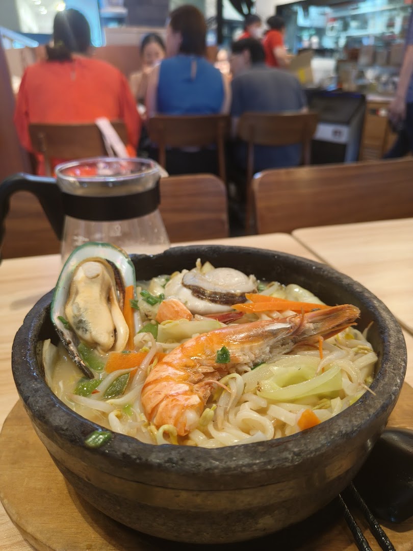 A steaming bowl of seafood ramen with shrimp, mussel, and vegetables on a wooden table in a restaurant.