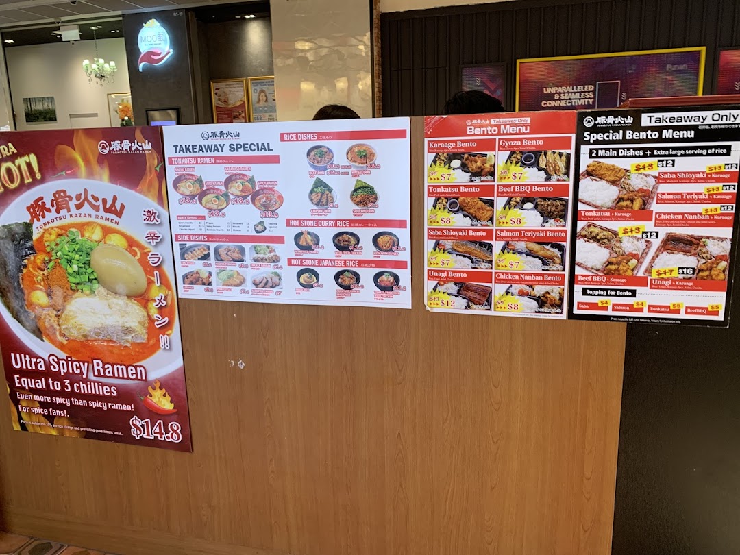 The entrance of Tonkotsu Kazan VOLCANO Ramen, featuring large promotional menus and a spicy ramen poster.
