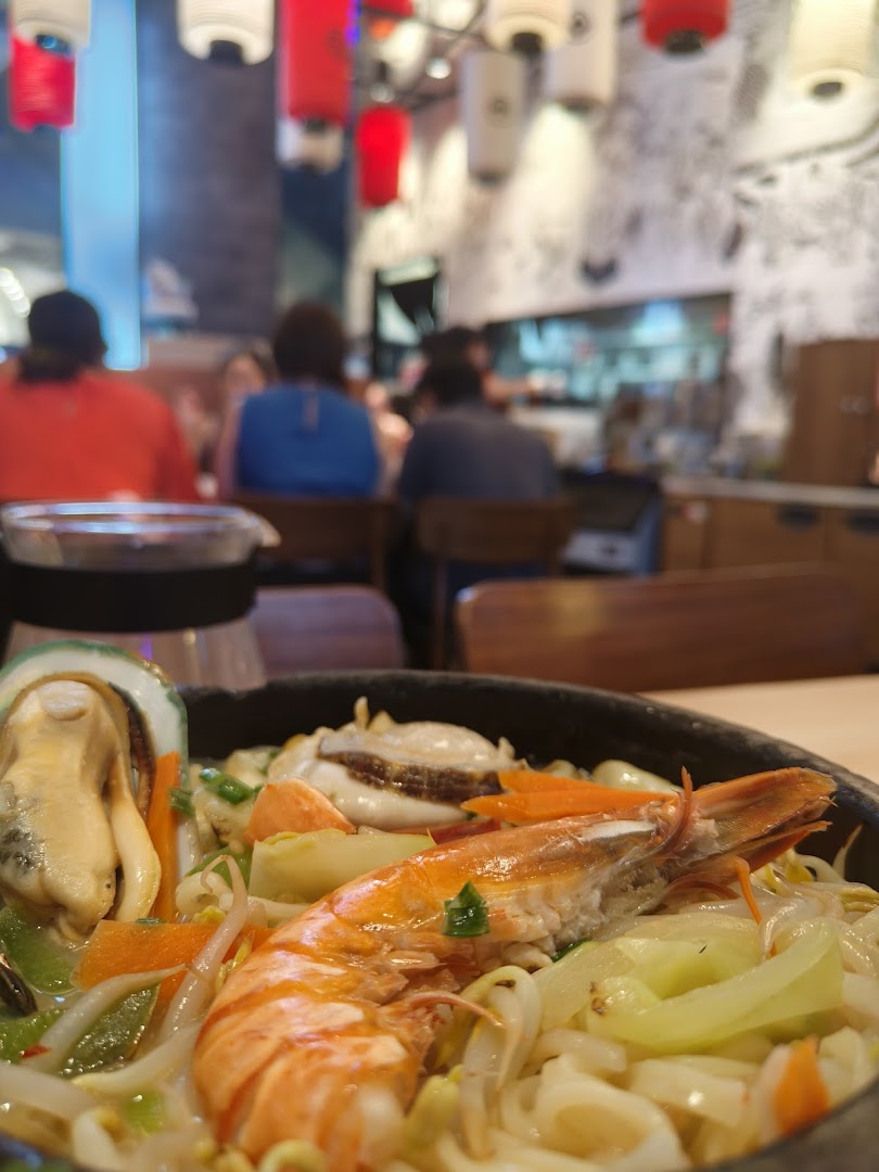 A close-up of a delicious seafood ramen dish with a vibrant restaurant interior and diners in the background.