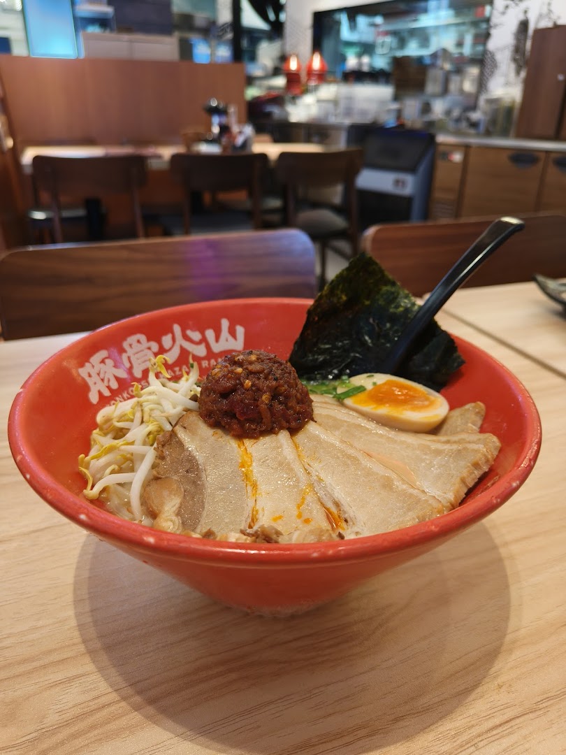 A vibrant red bowl of Tonkotsu Kazan ramen with pork slices, bean sprouts, egg, and spicy topping.