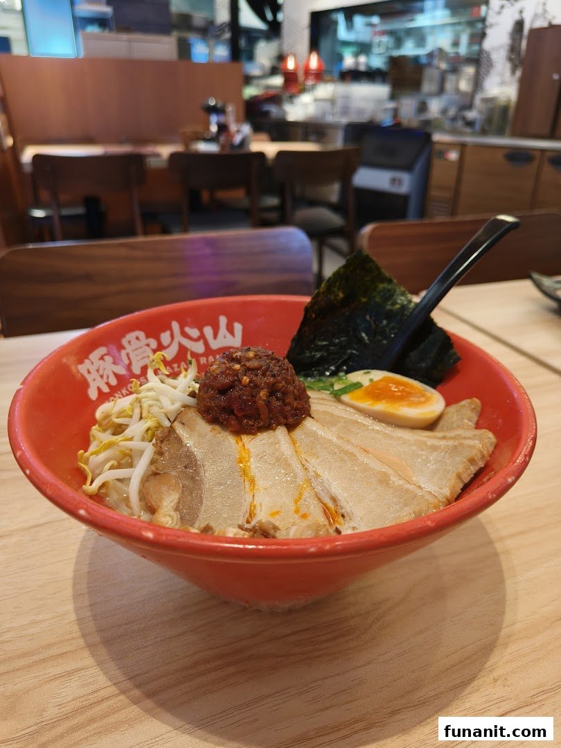 A vibrant red bowl of Tonkotsu Kazan ramen with pork slices, bean sprouts, egg, and spicy topping.