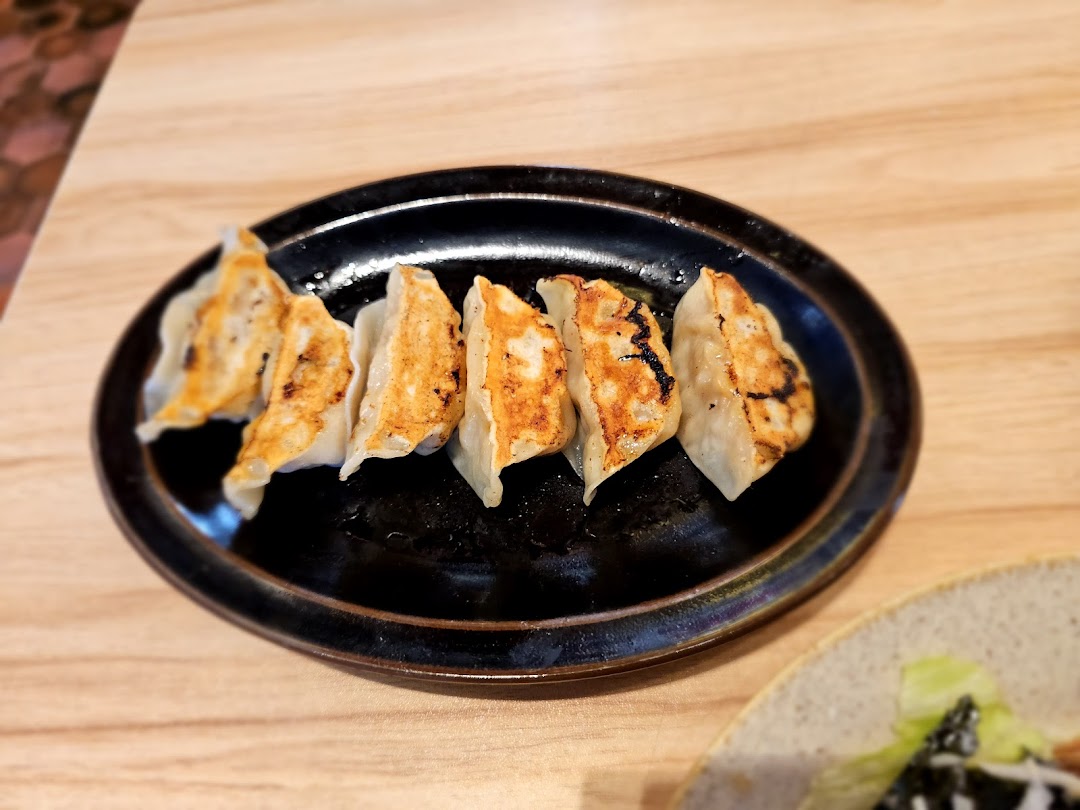 A plate of perfectly pan-fried gyoza with crispy bottoms, served on a dark oval dish.