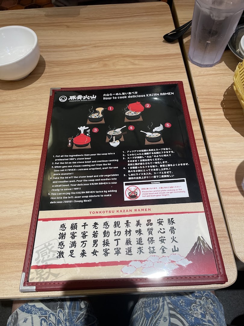 A laminated instruction sheet detailing how to enjoy Tonkotsu Kazan Ramen, placed on a wooden table.