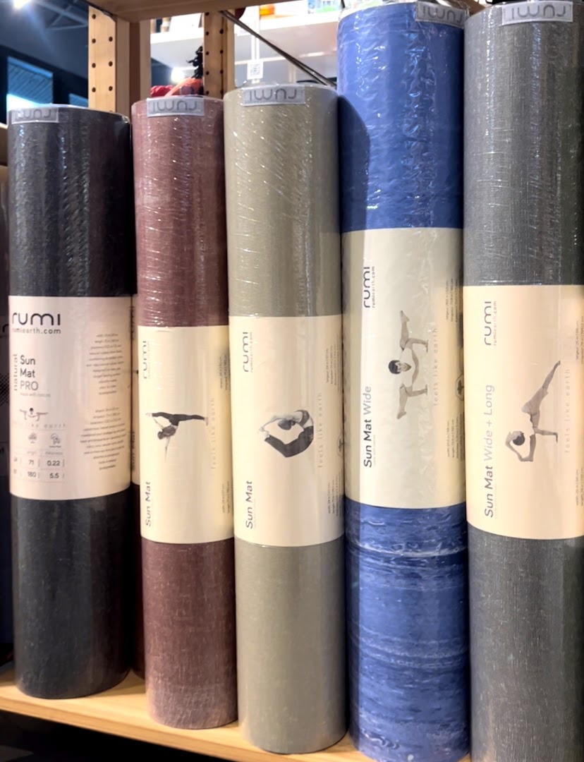 A display of colorful, rolled-up Rumi yoga mats on a shelf at Touch The Toes.