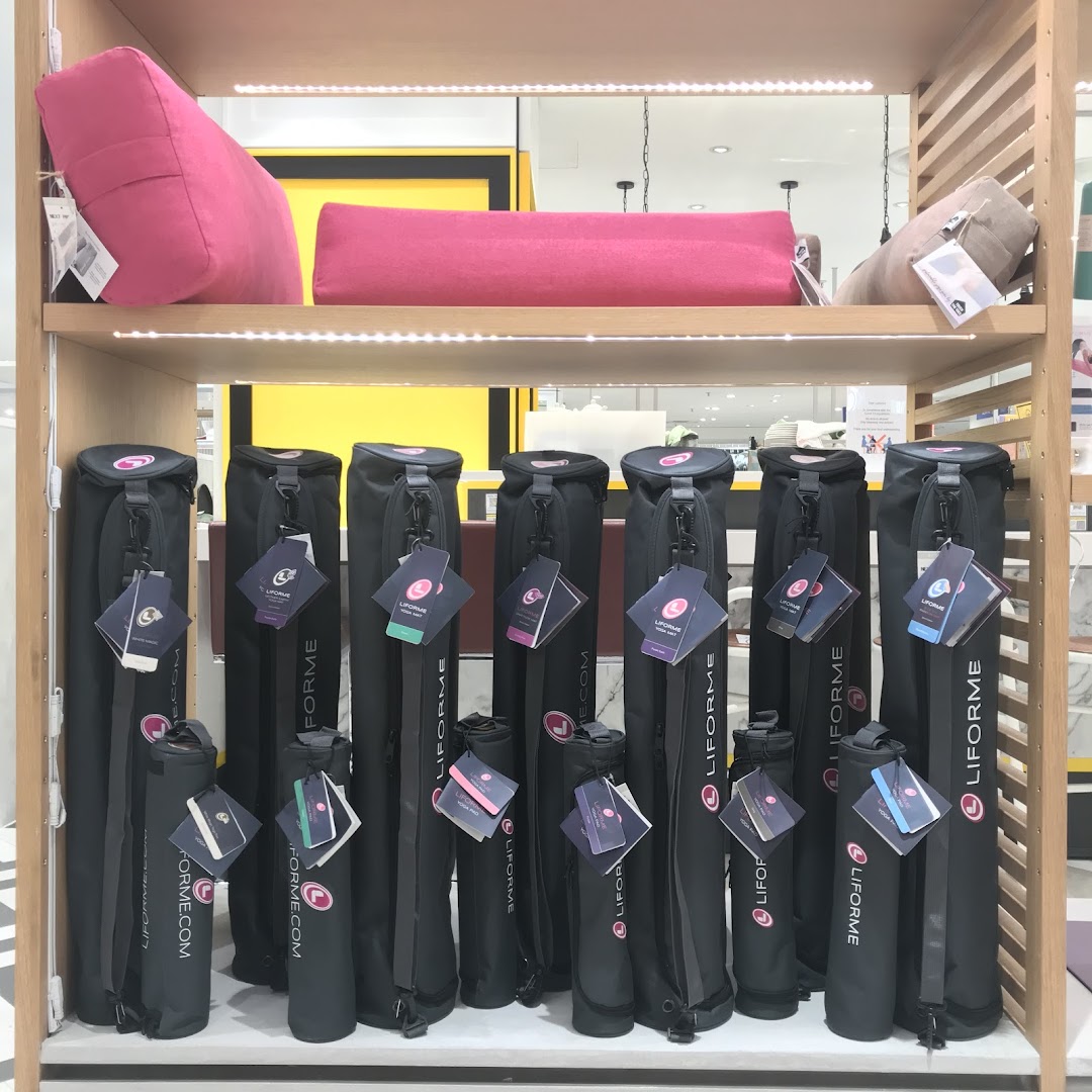 A retail display showcasing Liforme yoga mat bags and yoga bolsters on a wooden shelf.