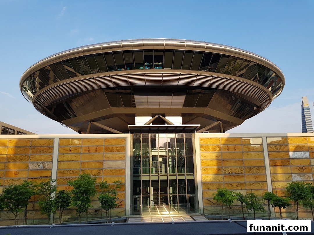 A modern, circular building with glass facades and a golden-patterned wall under a clear sky.