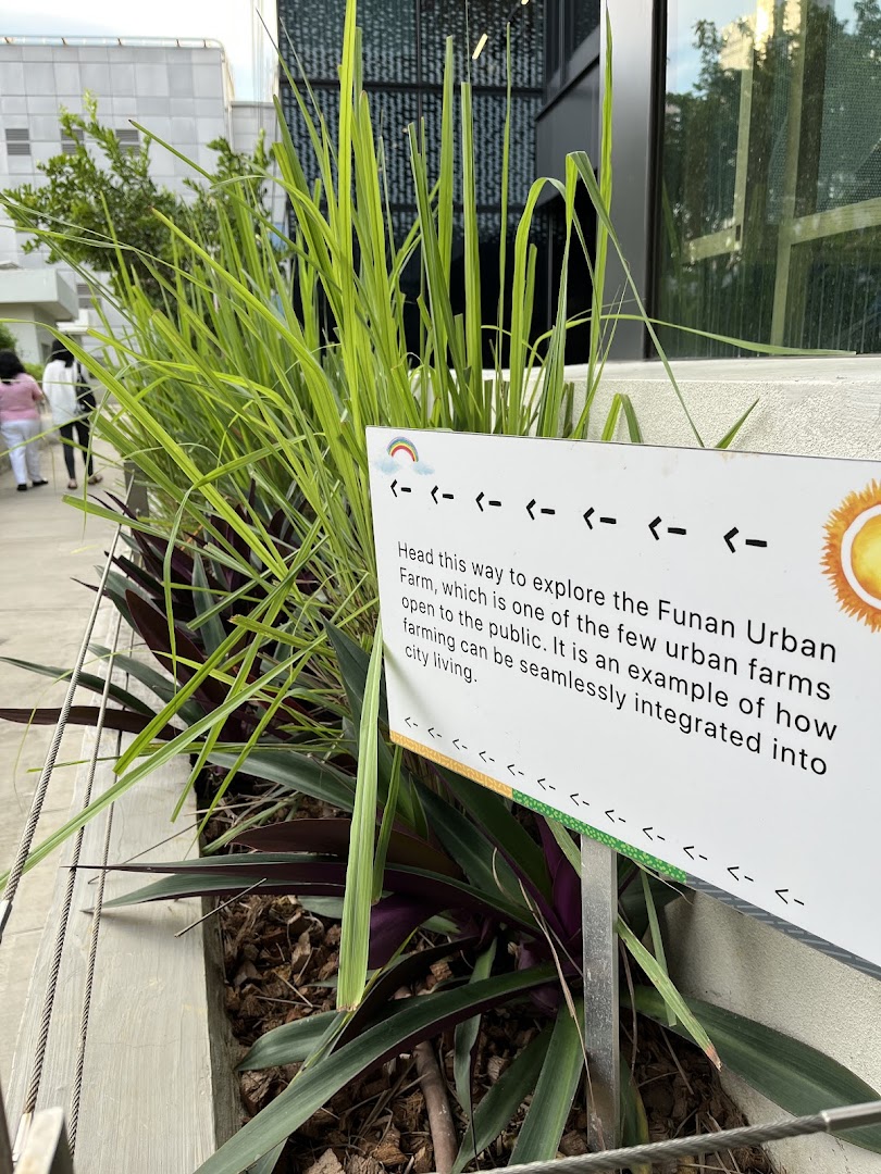 An informational sign guides visitors to the Funan Urban Farm amidst lush greenery.