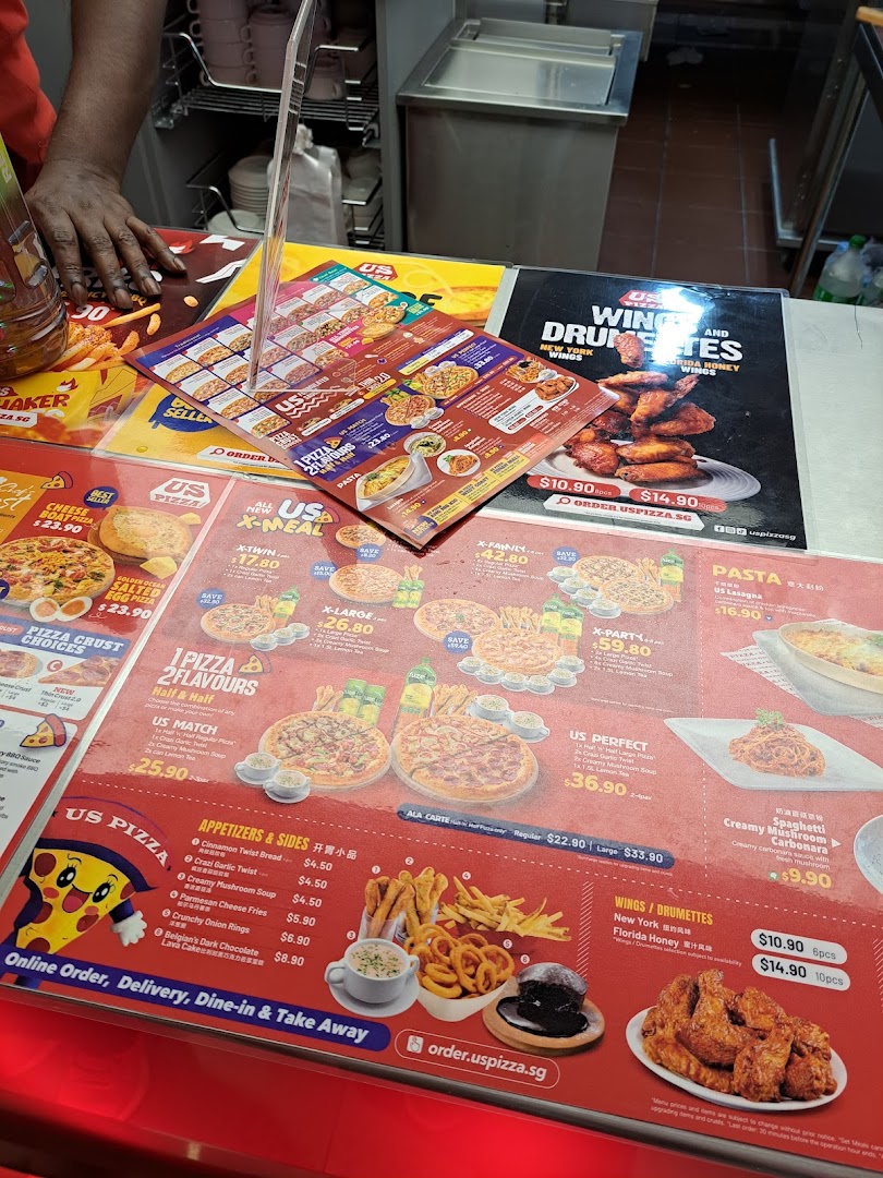A counter display showcasing US Pizza's extensive menu, including pizzas, sides, wings, and pasta.