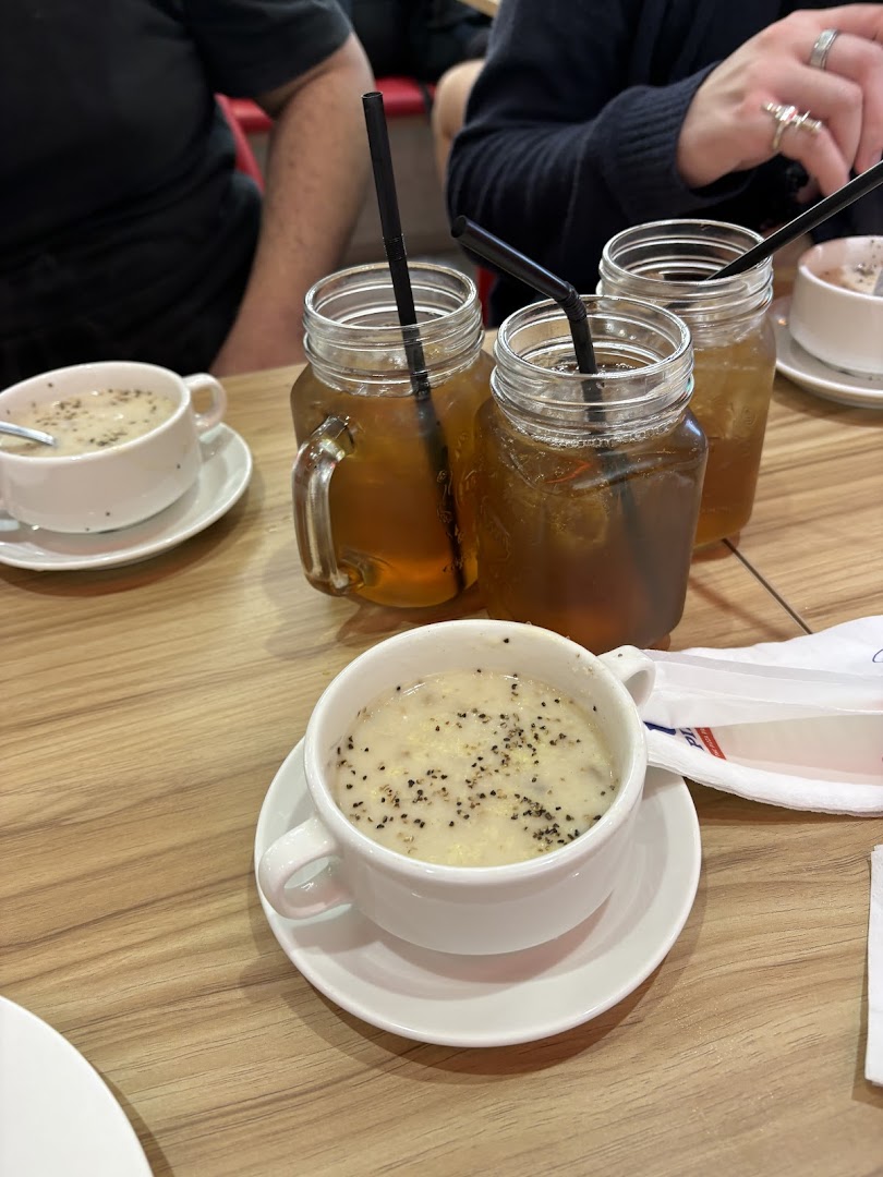 Multiple mason jar drinks and bowls of soup on a wooden table, with diners in the background.