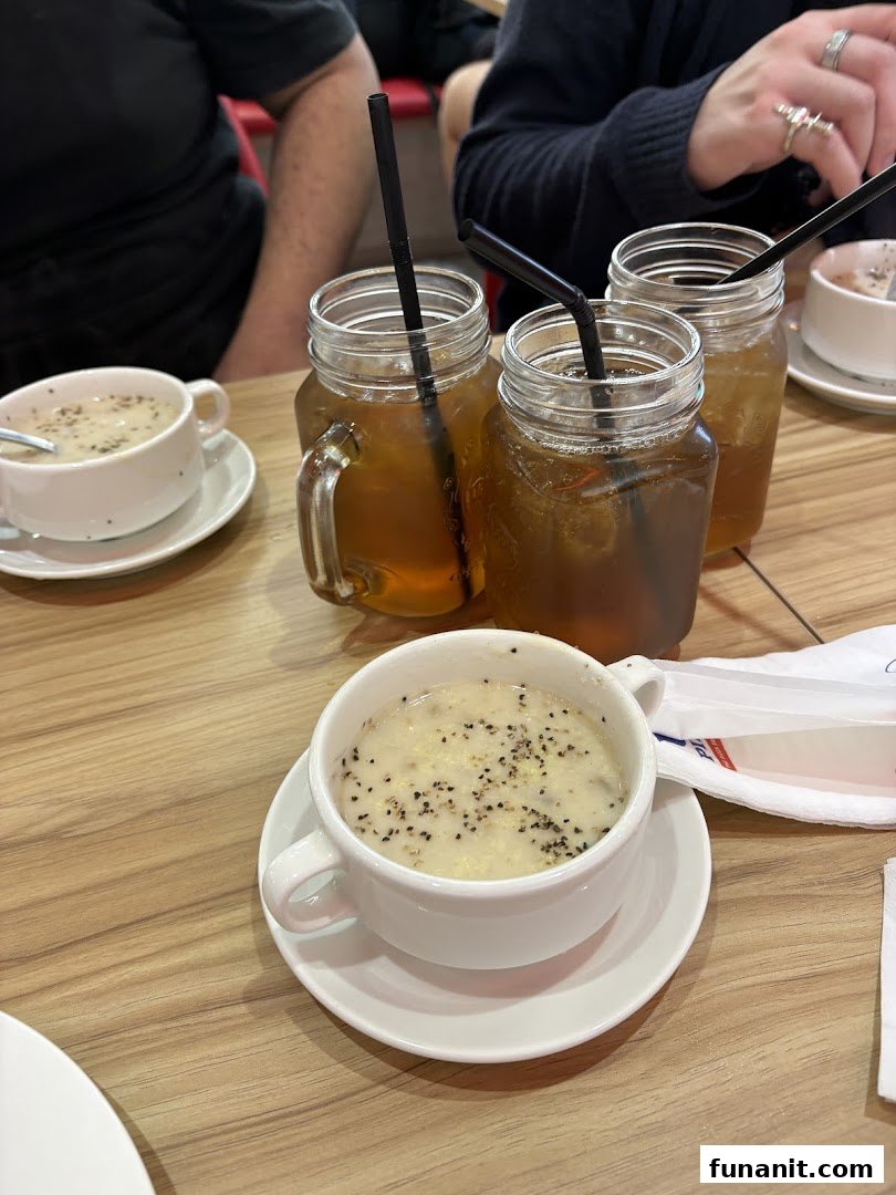 Multiple mason jar drinks and bowls of soup on a wooden table, with diners in the background.