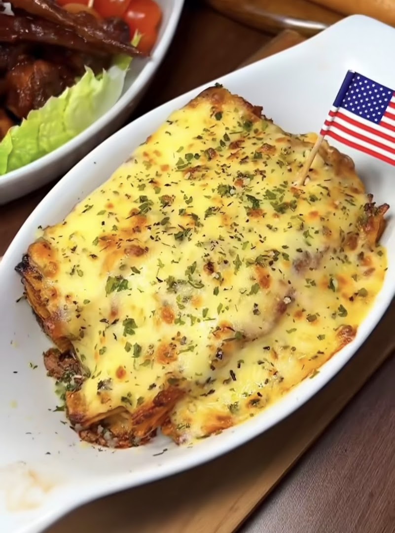 A cheesy baked dish, possibly lasagna, topped with herbs and an American flag pick.