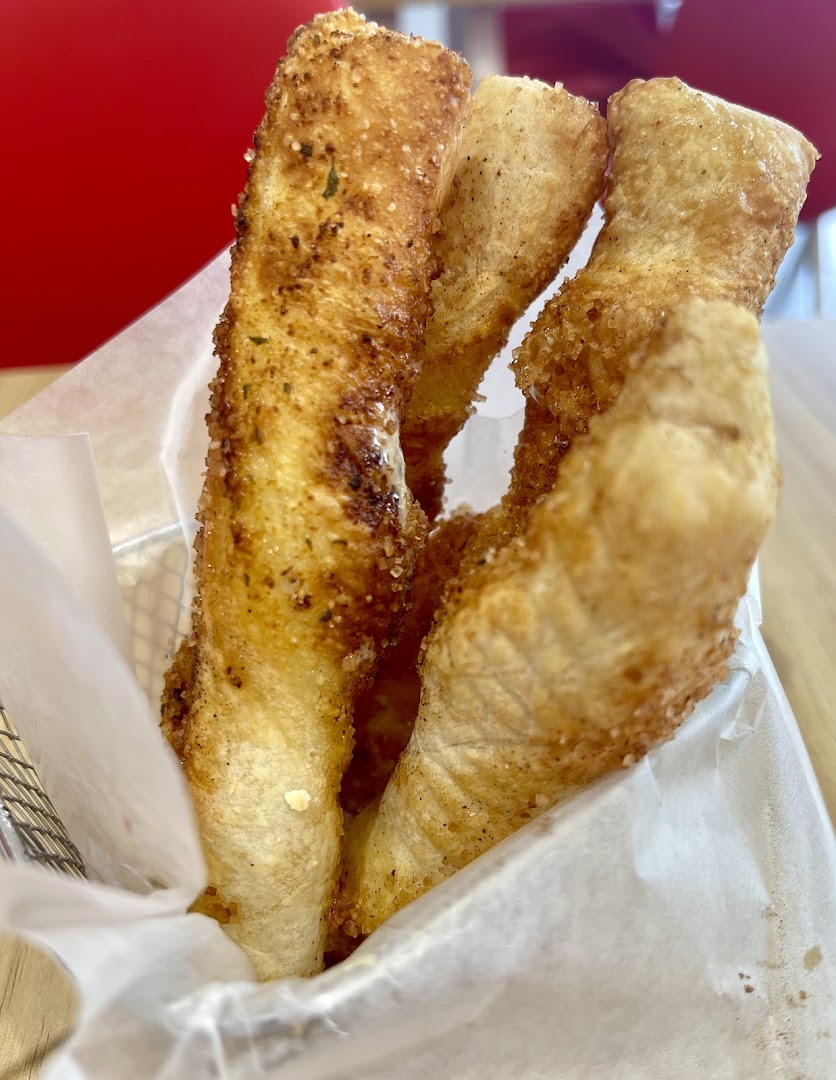 Close-up of golden-brown, seasoned breadsticks served in a metal basket with parchment paper.
