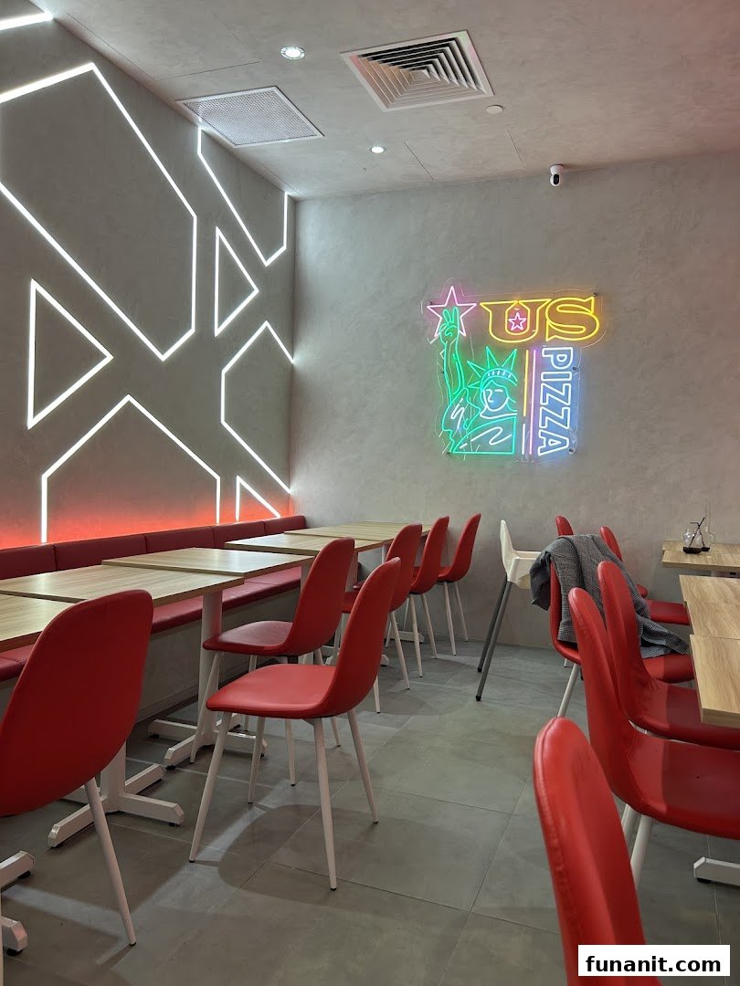 Interior view of US Pizza with red seating, wooden tables, and a vibrant neon logo.