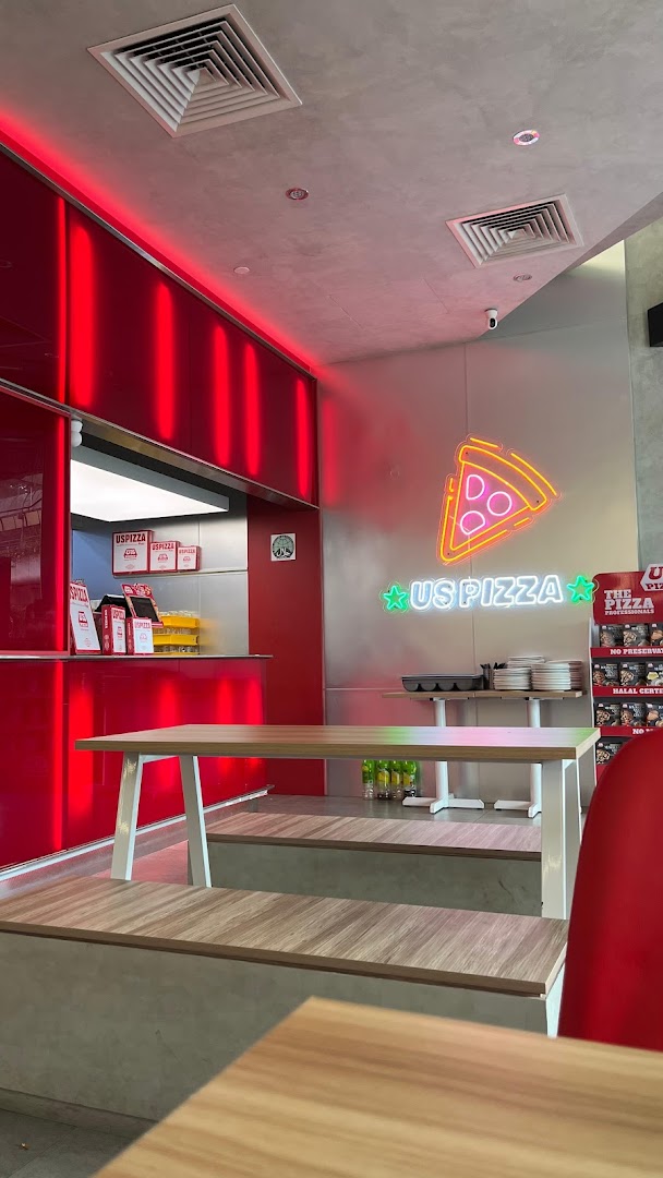 Vibrant interior of US Pizza featuring red accents, neon signage, and wooden seating.