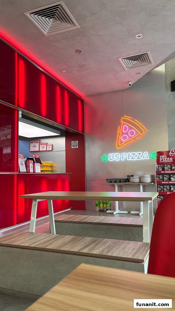 Vibrant interior of US Pizza featuring red accents, neon signage, and wooden seating.