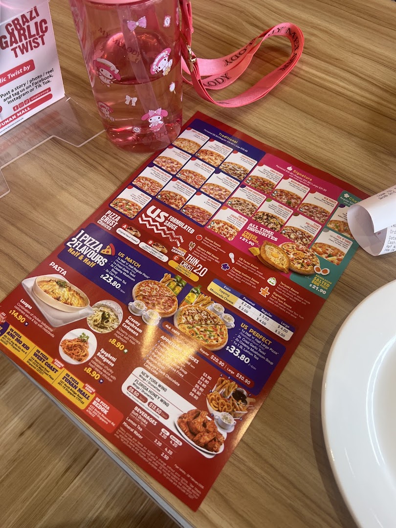 A detailed menu from US Pizza featuring various pizzas, pastas, sides, and beverages on a wooden table.