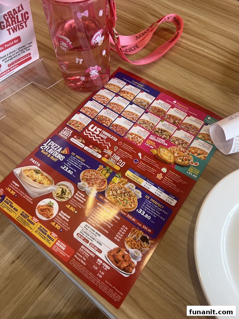 A detailed menu from US Pizza featuring various pizzas, pastas, sides, and beverages on a wooden table.