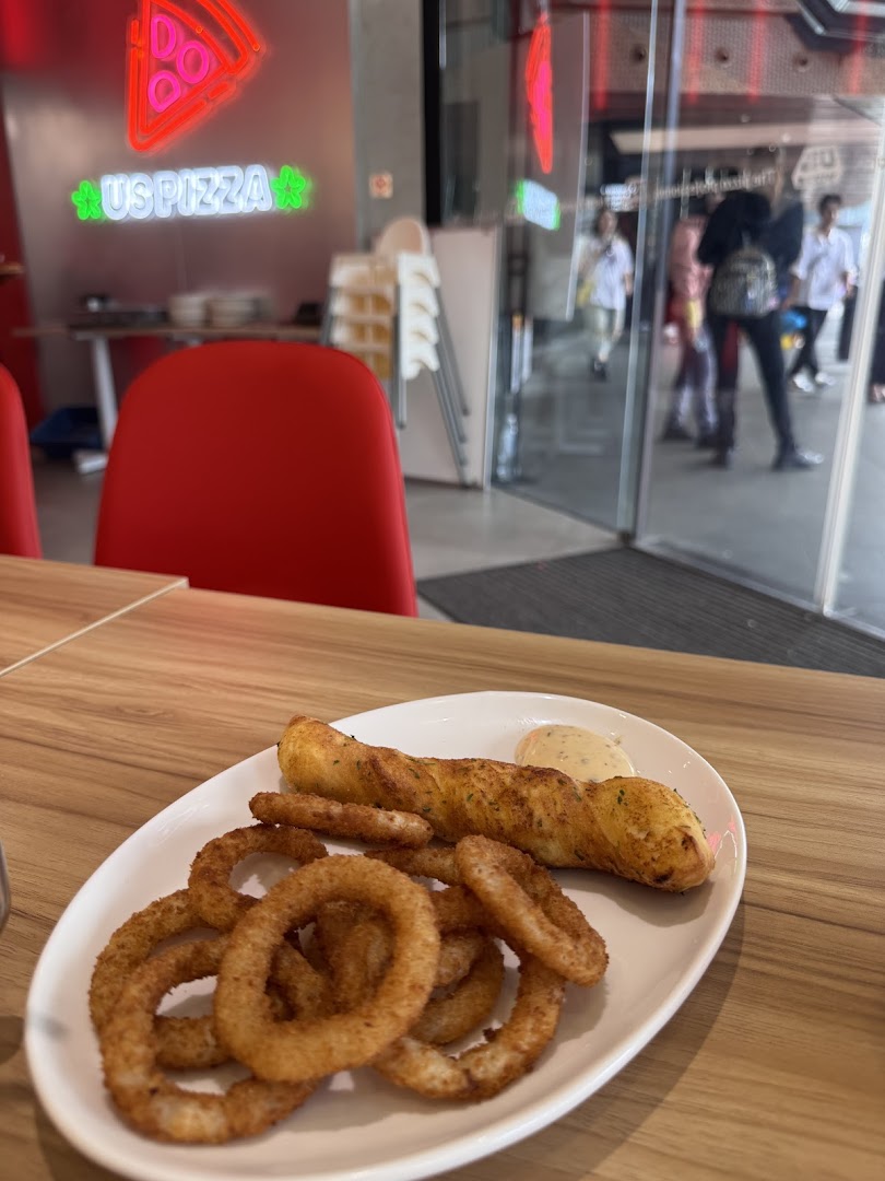 A plate of crispy onion rings and a breadstick with dip on a table inside US PIZZA.