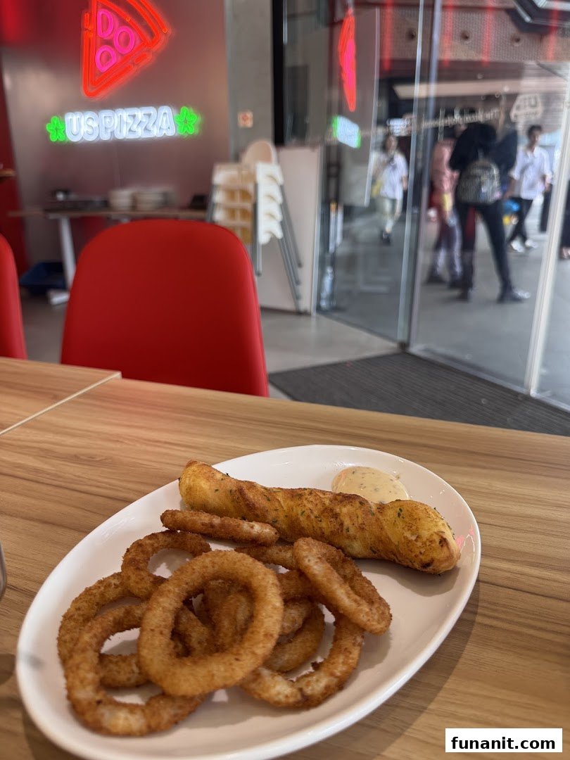 A plate of crispy onion rings and a breadstick with dip on a table inside US PIZZA.