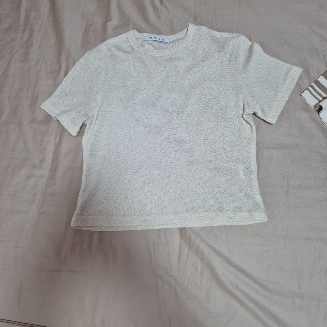 A light-colored, textured short-sleeved top from Wardrobemess, laid flat on a neutral surface.