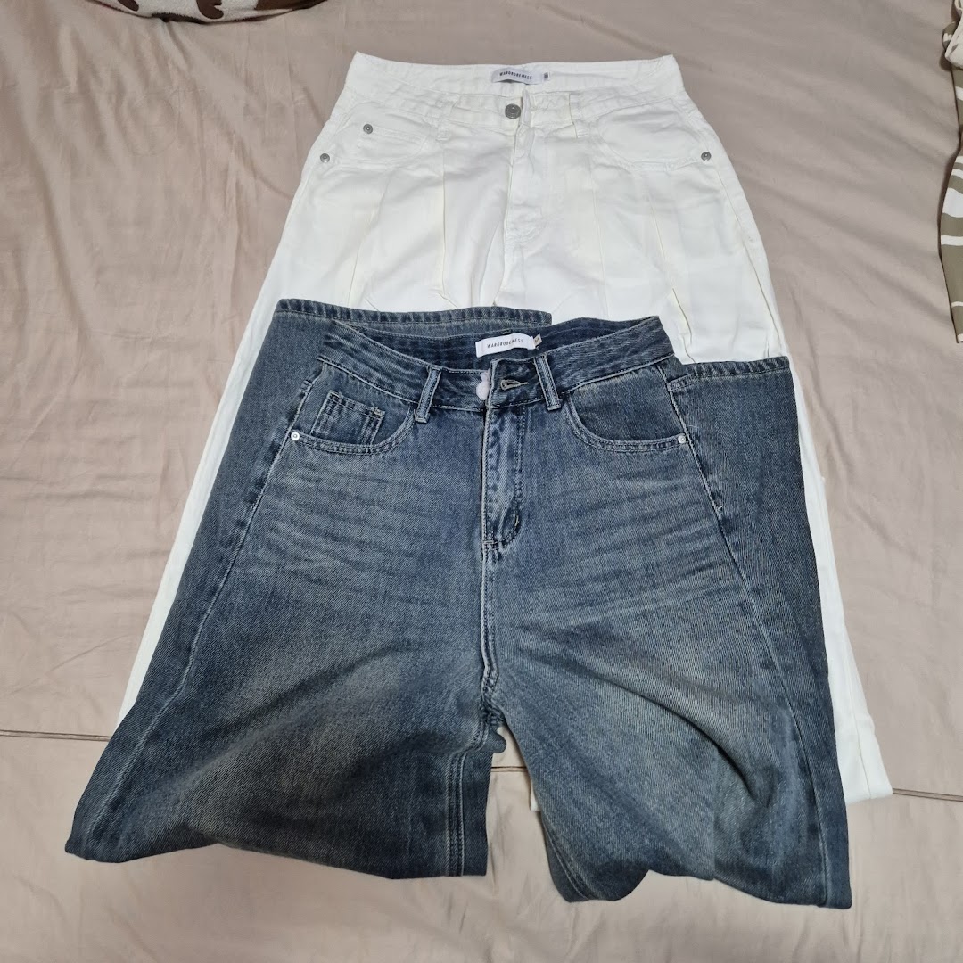 Two pairs of pants, one white and one blue denim, laid flat on a surface.