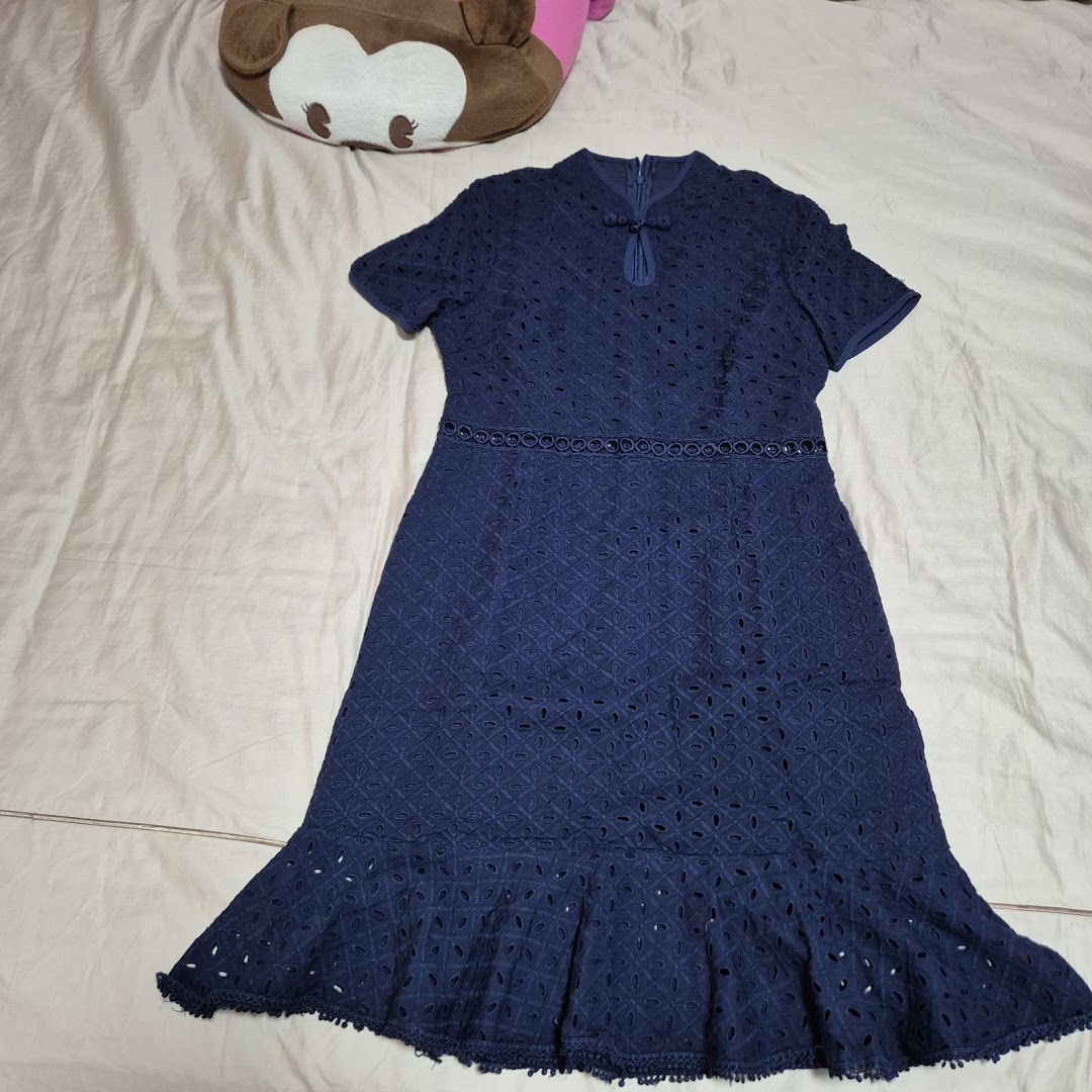 A navy blue eyelet dress with short sleeves and a ruffled hem, displayed on a bed.