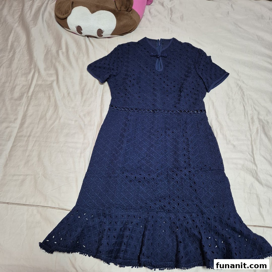 A navy blue eyelet dress with short sleeves and a ruffled hem, displayed on a bed.