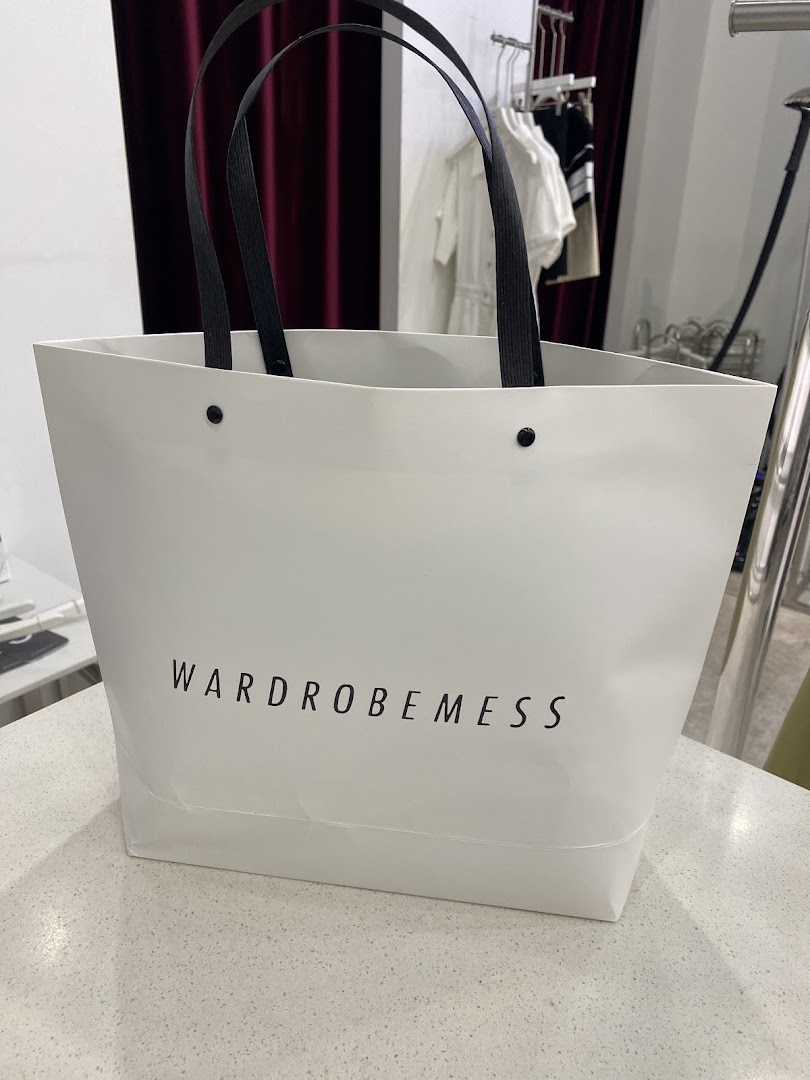 A white shopping bag with the 'WARDROBEMESS' logo, placed on a counter inside the store.