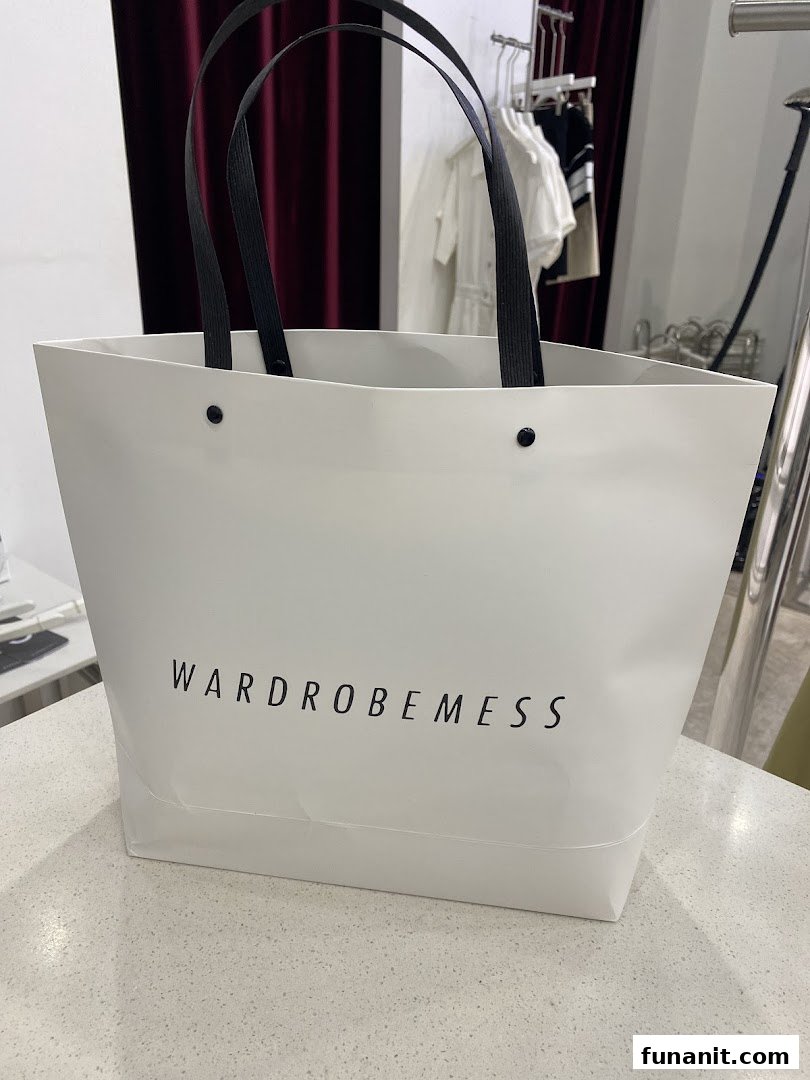 A white shopping bag with the 'WARDROBEMESS' logo, placed on a counter inside the store.