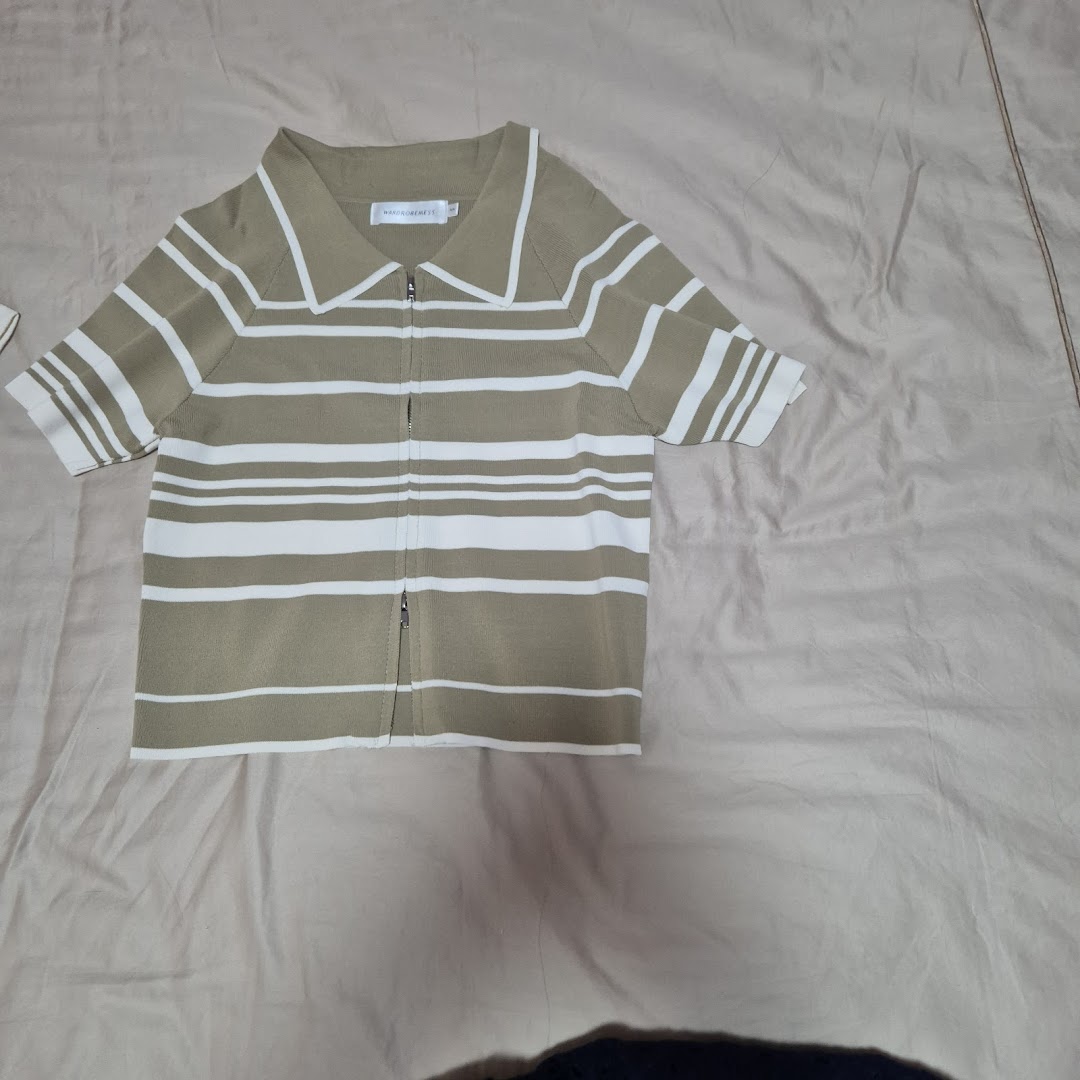 A beige and white striped knitted polo top with a full-length zipper, displayed on a light fabric.