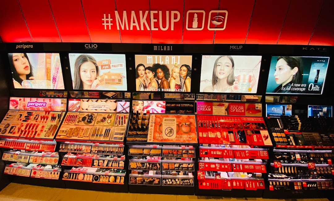 A vibrant display of makeup products from various brands like Peripera, Clio, Milani, and MKUP.