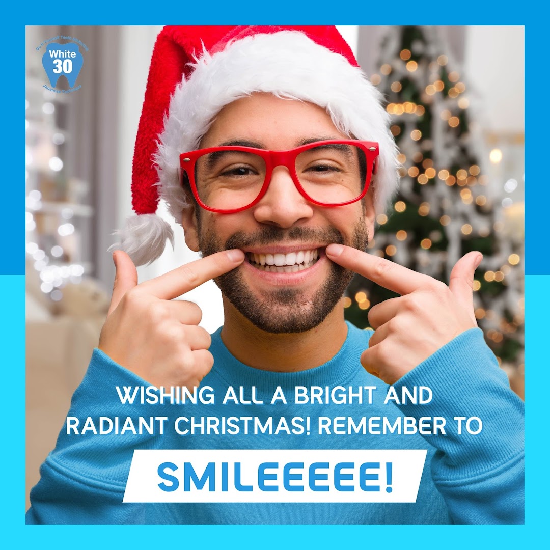 A man in a Santa hat points to his bright smile, wishing a radiant Christmas.