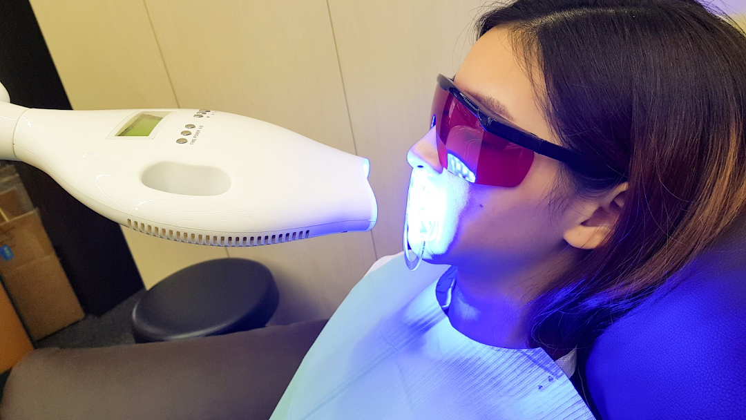 A person undergoing a teeth whitening treatment with a blue light device and protective eyewear.