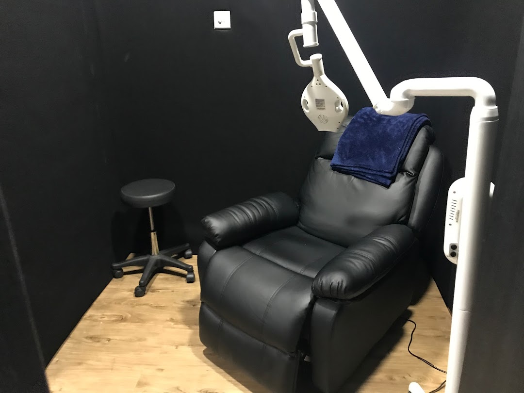 A comfortable black recliner chair with a blue blanket and professional teeth whitening equipment in a private room.