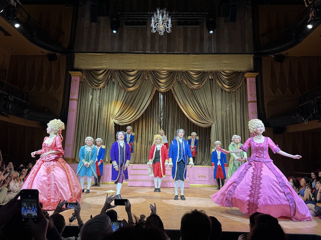 Performers in elaborate 18th-century costumes on stage at Wild Rice Funan, with an audience watching.