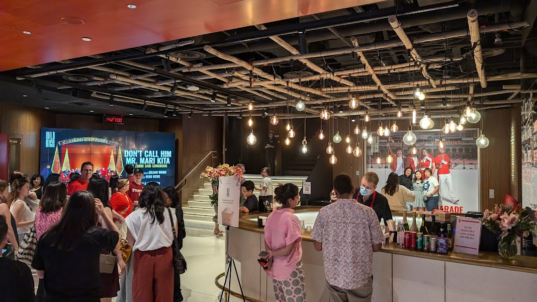 A vibrant theatre lobby at Wild Rice Funan, featuring a bar, large screen, and patrons gathering.