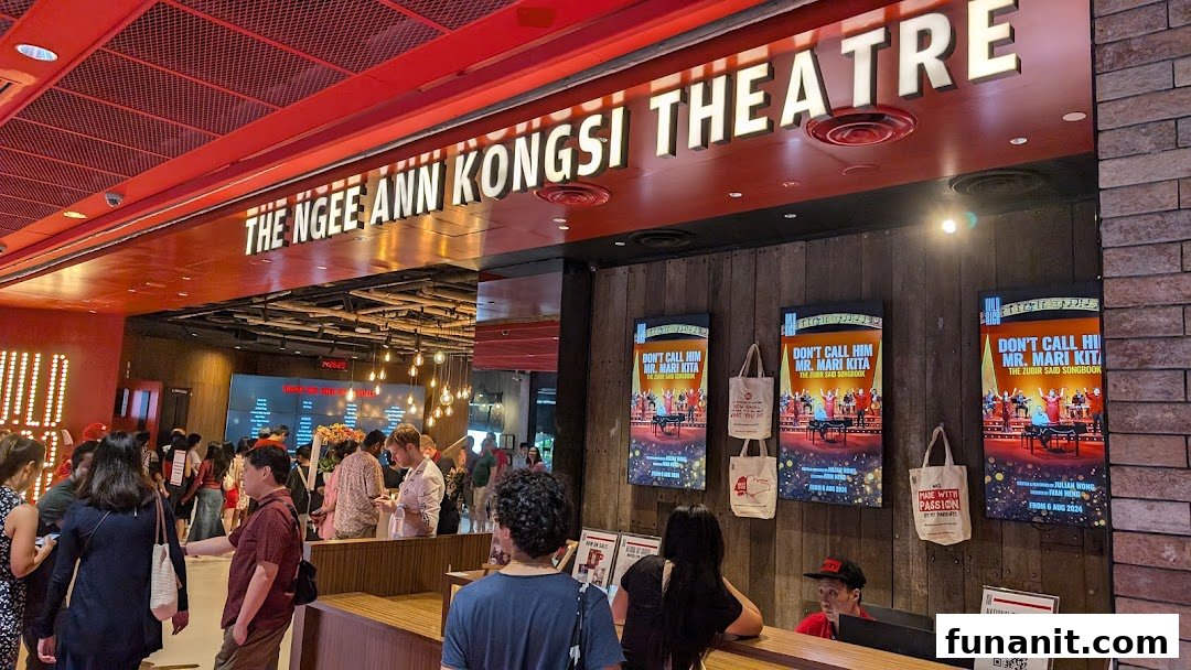 A bustling theatre lobby with patrons, a reception desk, and promotional posters for upcoming shows.