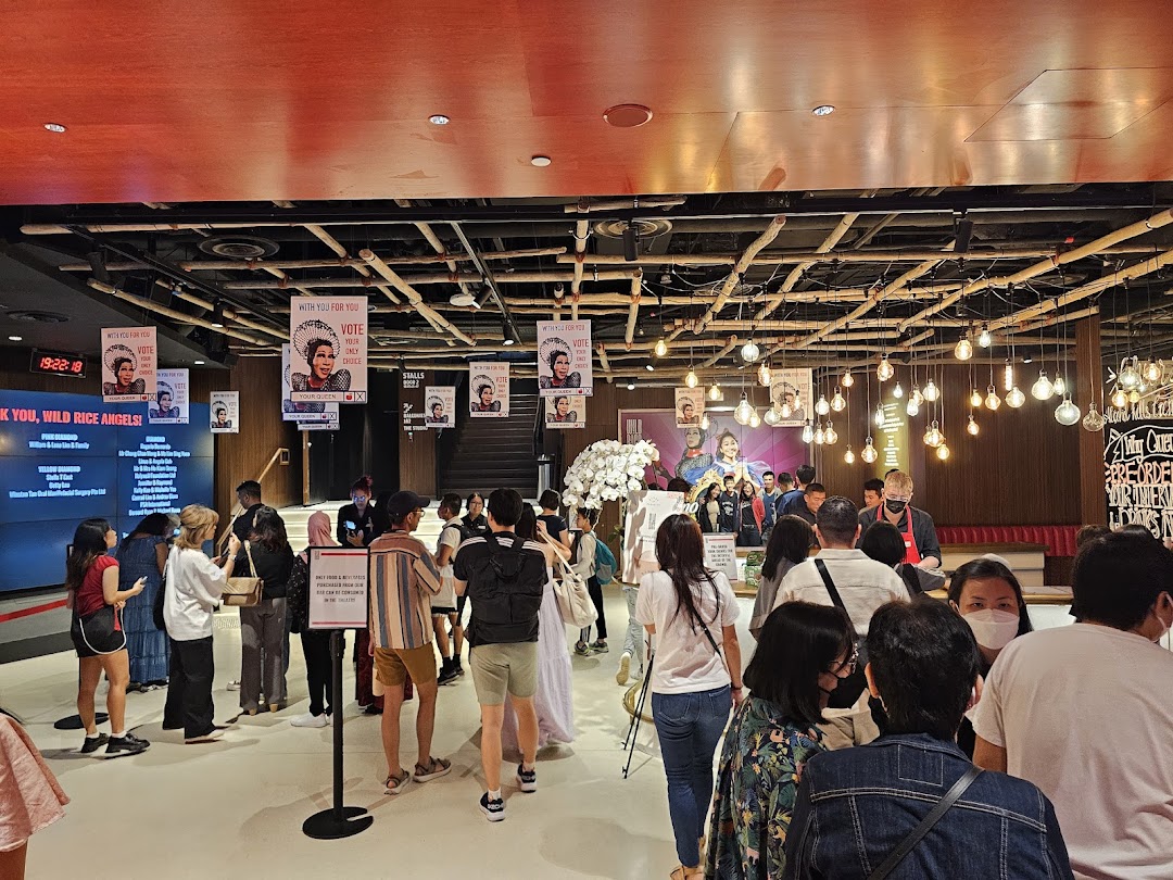 A lively interior scene at Wild Rice Funan, featuring a crowd, large screen, and unique decor.