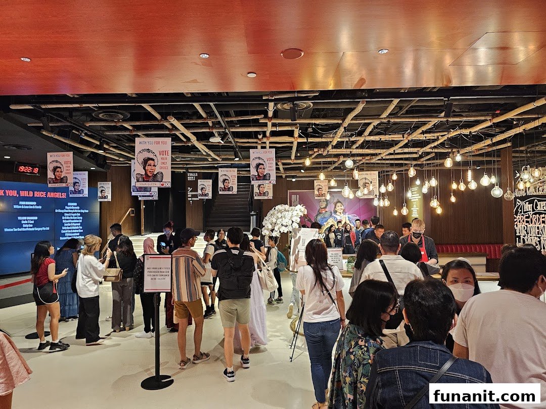 A lively interior scene at Wild Rice Funan, featuring a crowd, large screen, and unique decor.