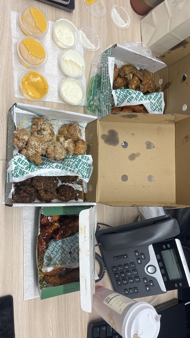 An overhead view of various Wingstop chicken wings, boneless bites, and dipping sauces in takeout boxes.