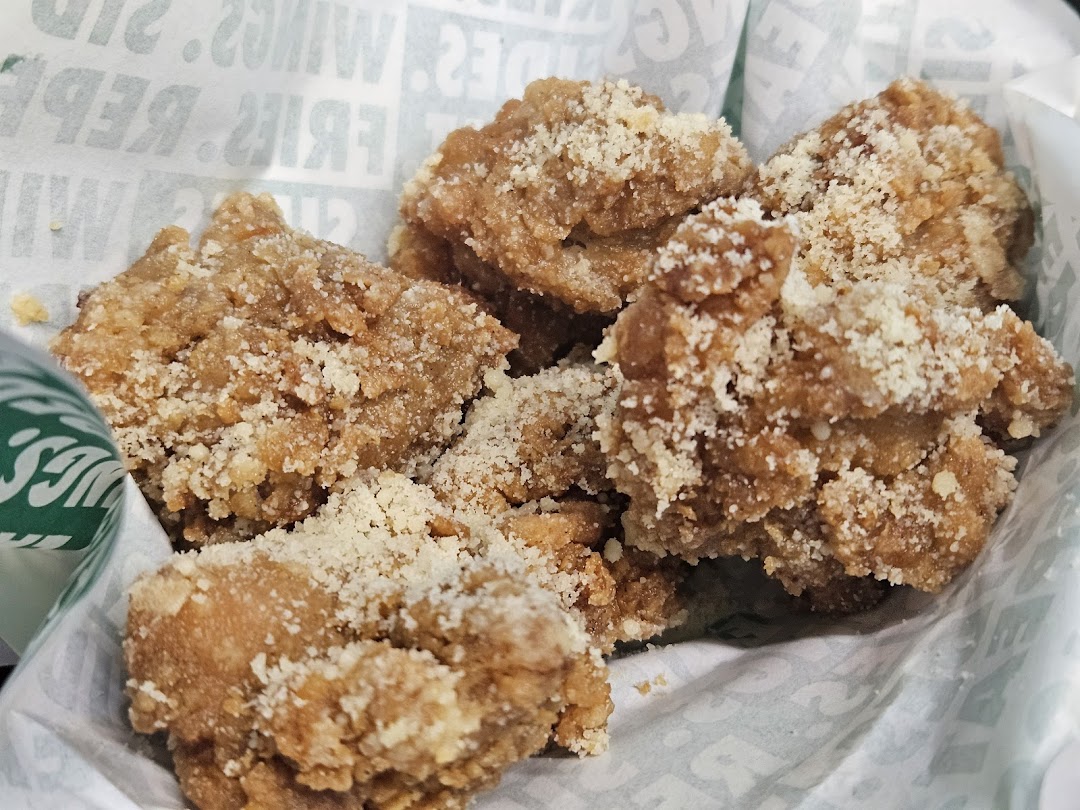 Close-up of crispy, golden-brown boneless chicken pieces topped with parmesan cheese in a Wingstop basket.
